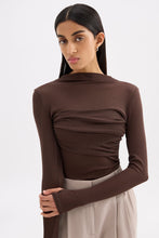 Model posing in the chocolate top with arms crossed, highlighting the raised neckline and extended sleeves.