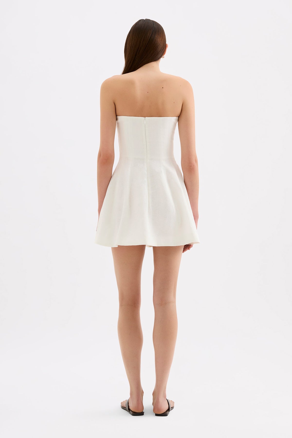 White mini dress shown from the back, featuring a strapless neckline, fitted bodice, centre-back zip and flared skirt.