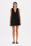 A model wears the black mini dress in a full front studio view, showing the deep V neckline, gathered detailing and loose full skirt.