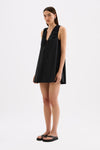 The model wears the black mini dress in a three-quarter front view, showing the deep V neckline, front tie and relaxed A-line shape.