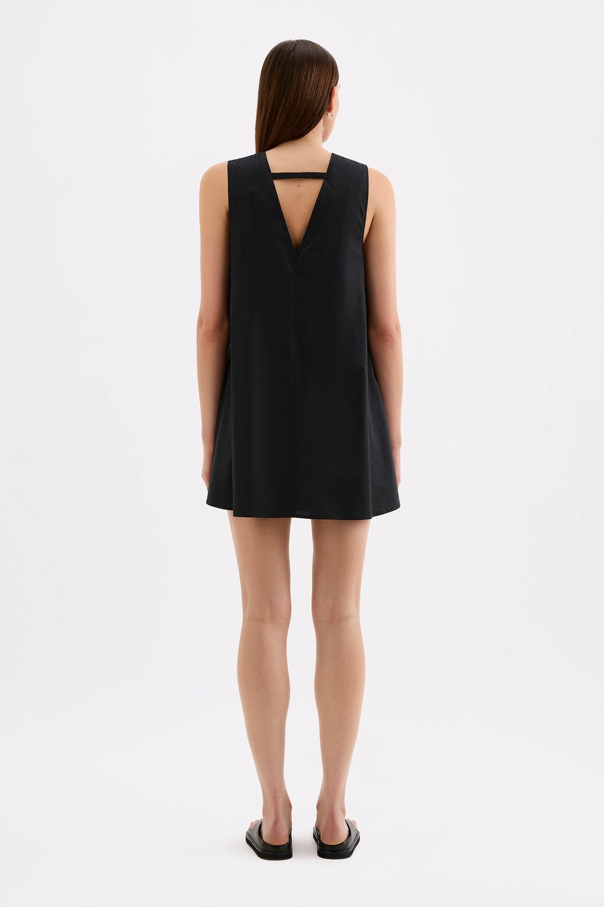 Back view of the black mini dress showing the wide shoulder straps, triangular back cut-out and loose full skirt.