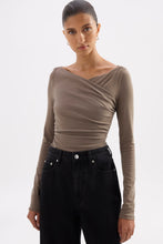 Model wearing the truffle draped long sleeve top in a relaxed angled pose with black wide-leg jeans.