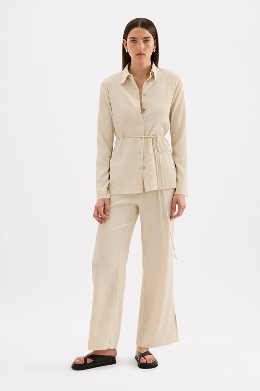 Full-length front view of the cream relaxed pants styled with the matching shirt and black sandals.