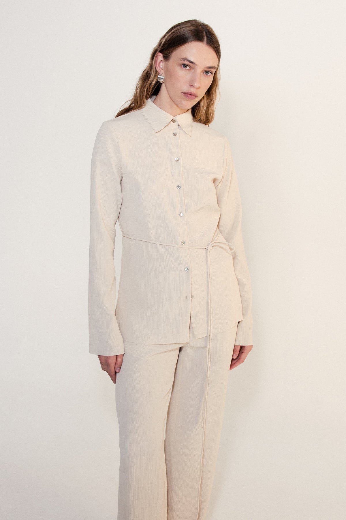 Product-only front view of the cream long sleeve shirt with traditional collar, shell buttons and waist tie.