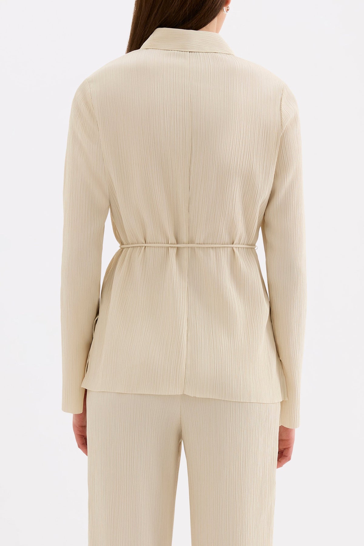 Back view showing the clean long sleeve silhouette and cinched waist of the cream shirt.