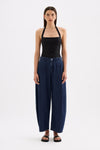 A model wears indigo blue wide-leg denim pants with deep pleats and a high waist in a full front studio view.