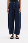 Close-up front view of the indigo blue denim pants showing the waistband, button closure, front pleats and side pockets.
