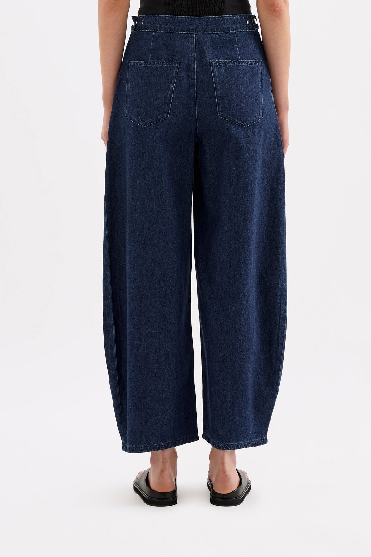 Close-up back view of the indigo blue denim pants showing the adjustable waist tab, back pocket and waistband details.