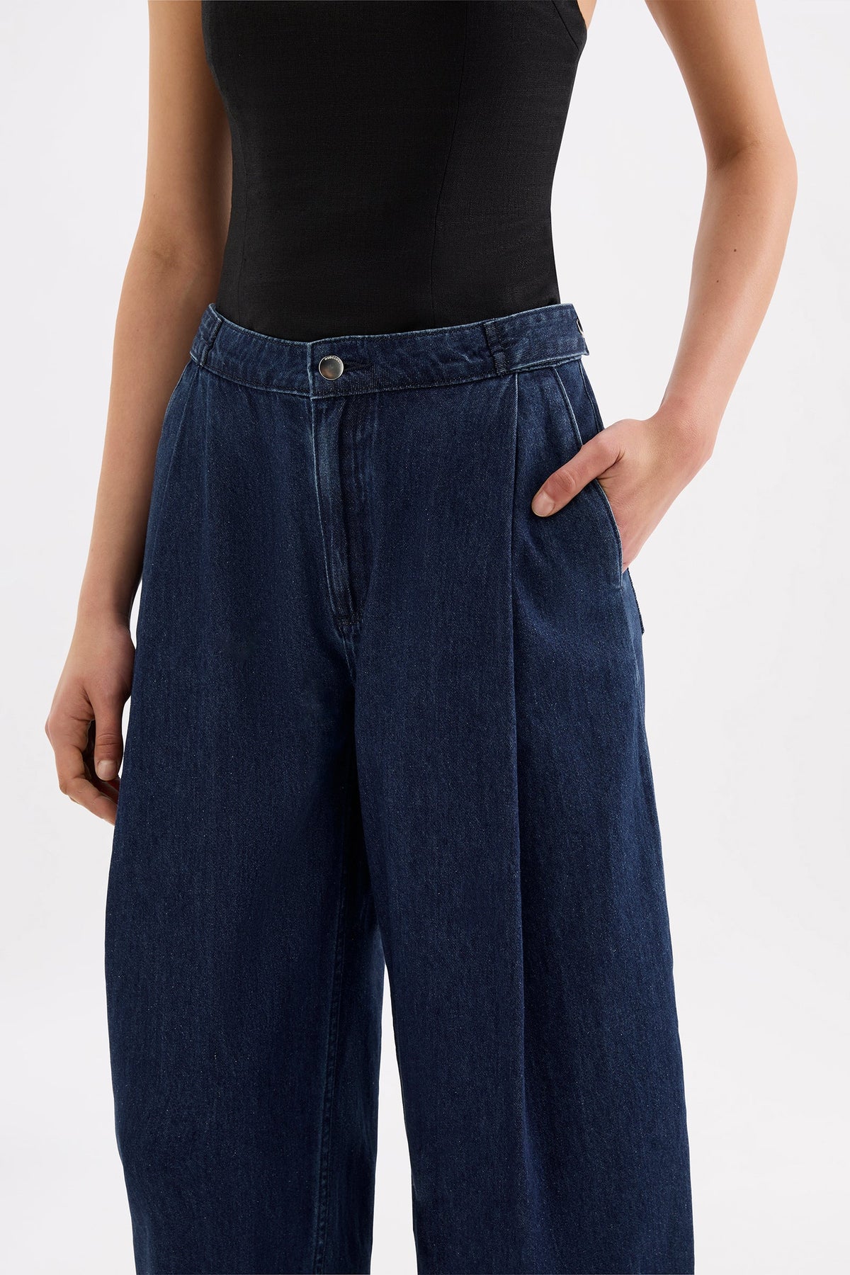Close-up front view of the indigo blue denim pants showing the button fastening, waistband, front pleats and side pocket.