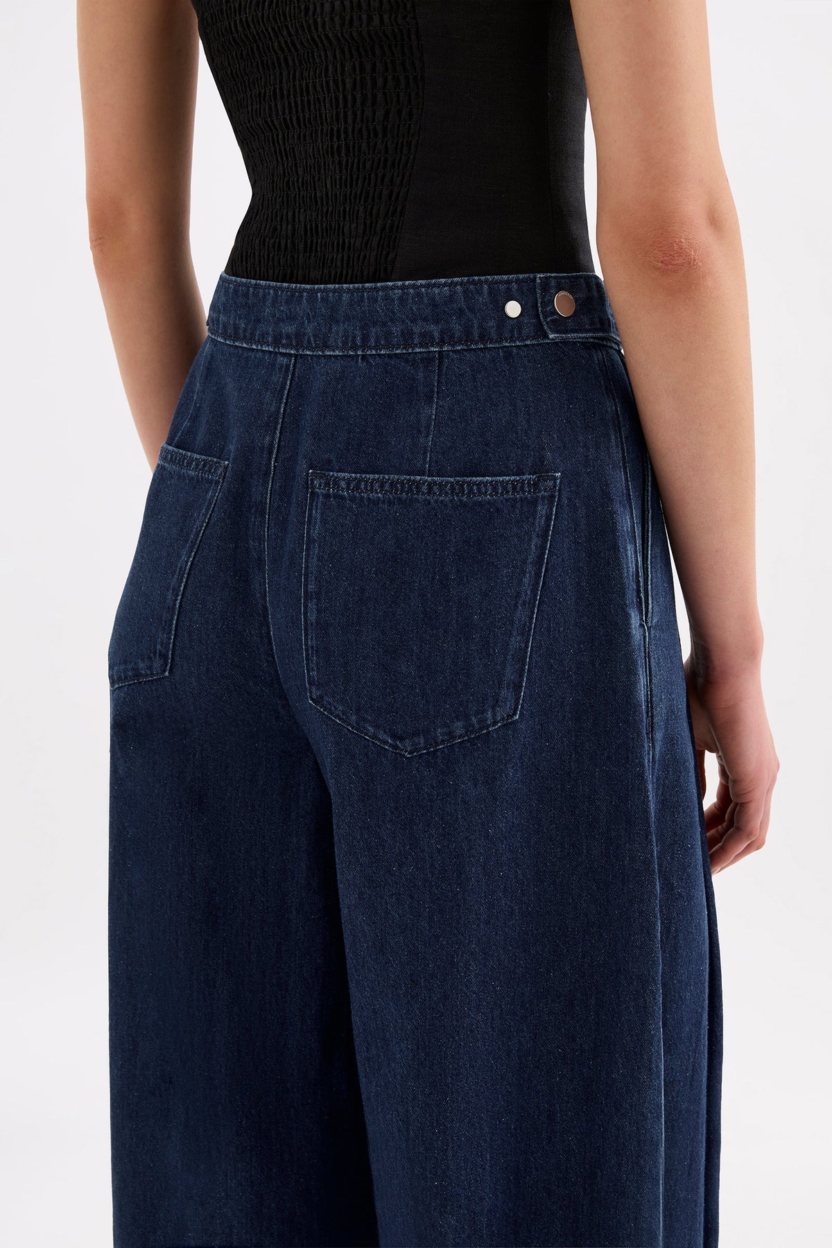 Close-up back view of the indigo blue denim pants showing the adjustable waist tab, back pocket and waistband details.