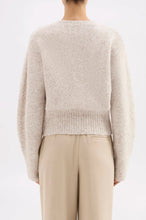 Person wearing a light beige sweater and beige pants on a white background