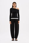 Full-length front view of the fitted black long sleeve top with asymmetrical neckline and white contrast layer, styled with black pants.