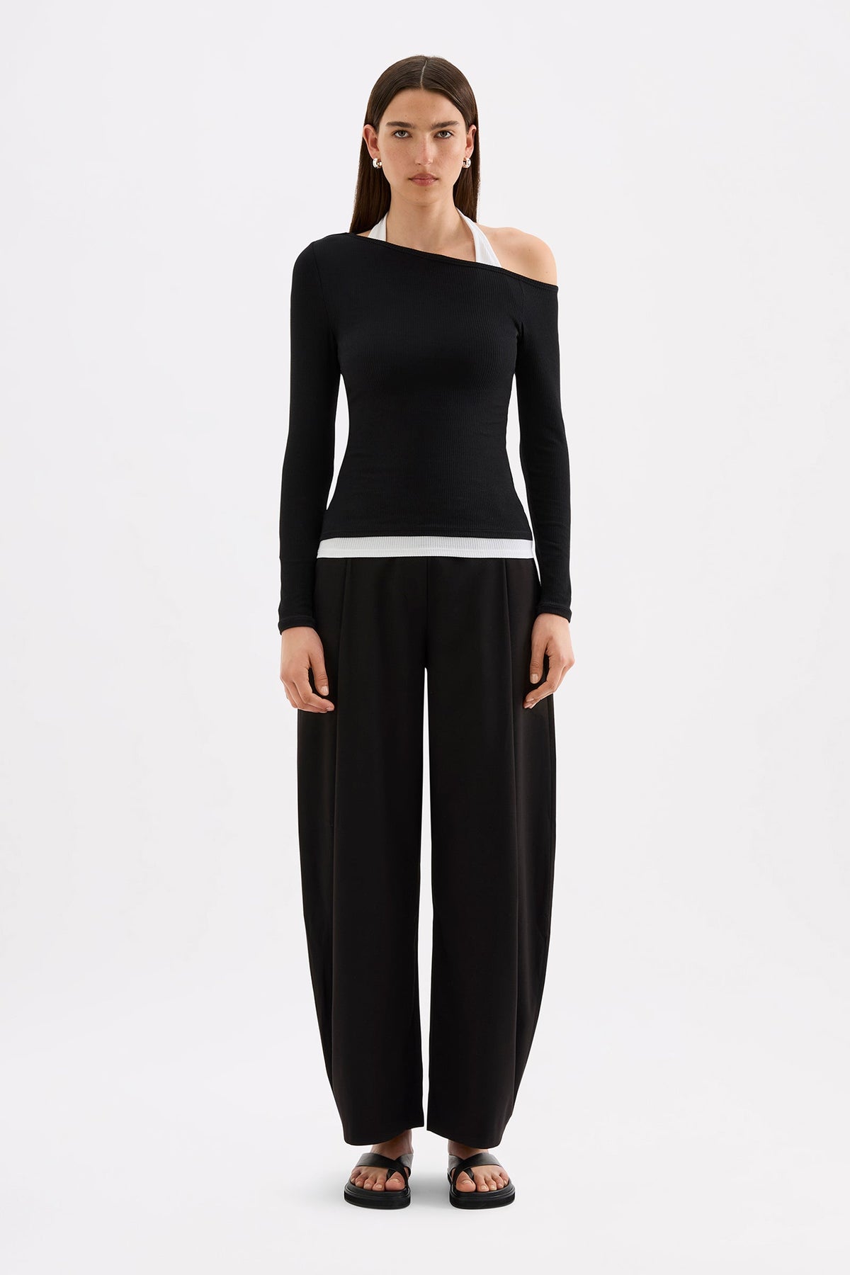 Full-length front view of the fitted black long sleeve top with asymmetrical neckline and white contrast layer, styled with black pants.