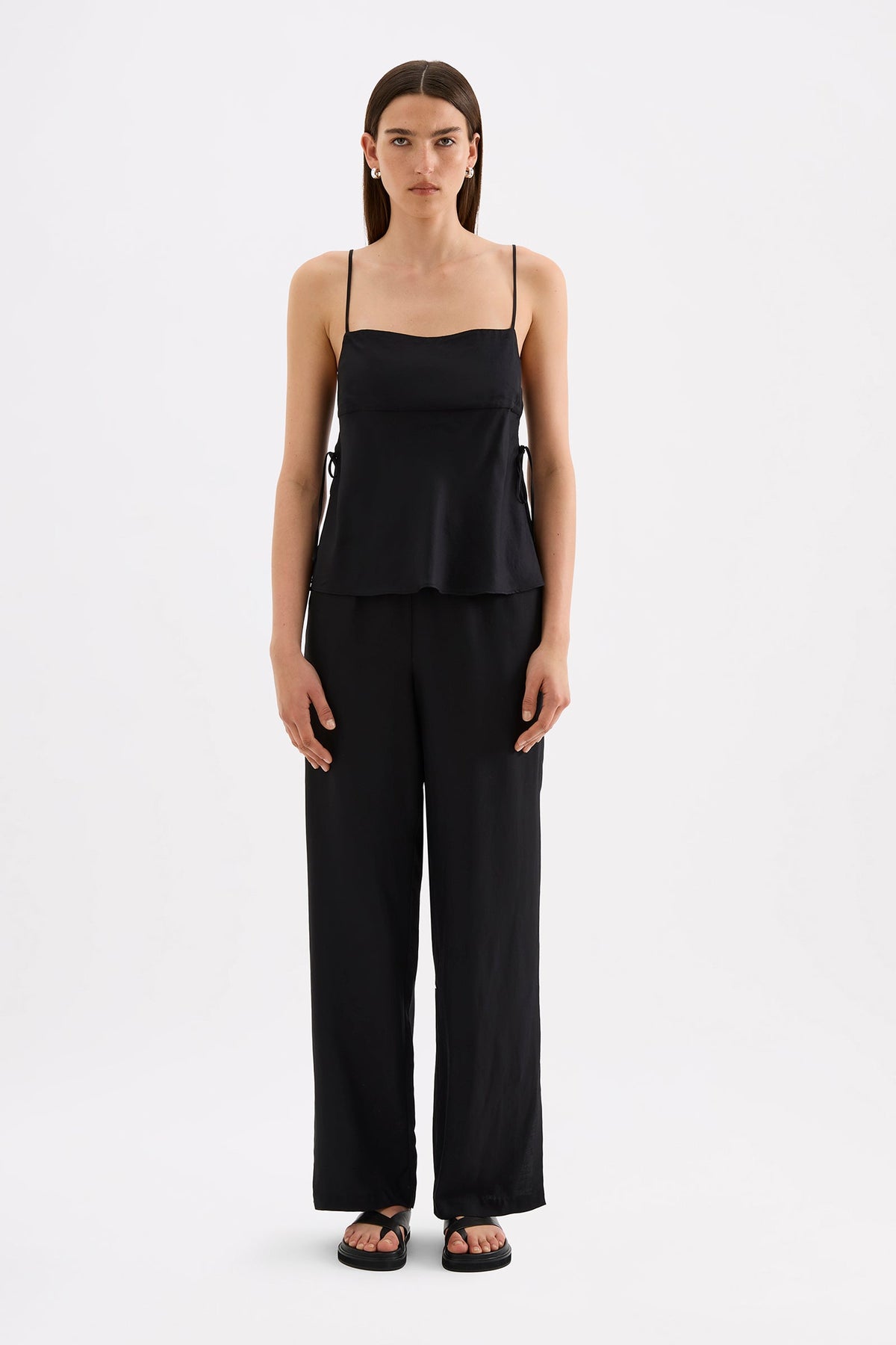 A model wears a black cami top with thin adjustable straps and wide side panels in a full front studio view.