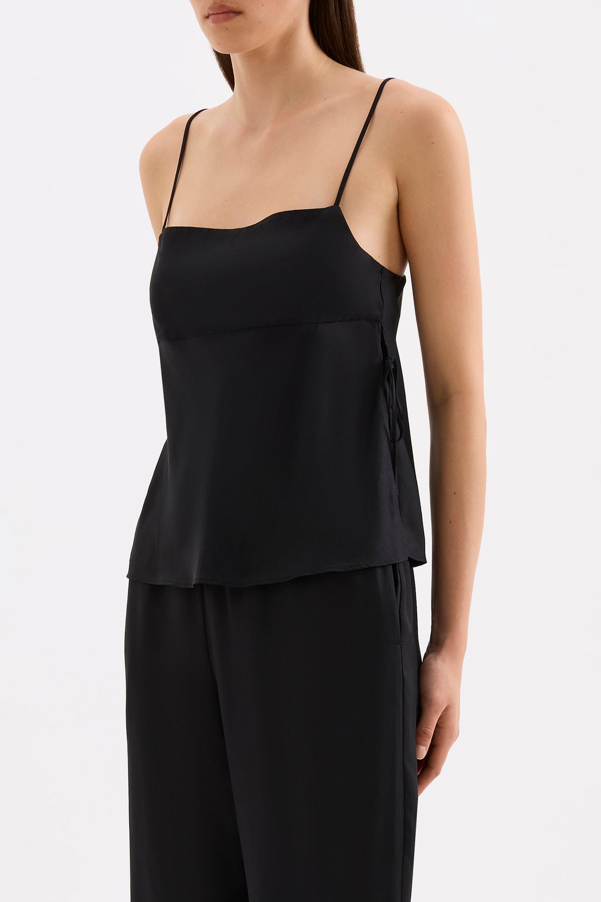 Three-quarter view of the black cami top showing the relaxed silhouette and wide side split with tie detail.