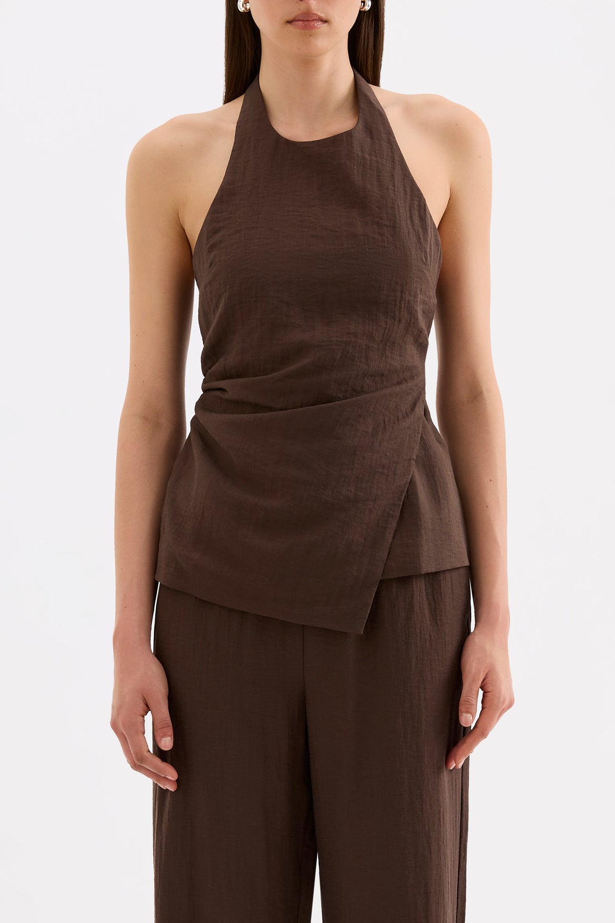 Front close-up showing the high halter neckline, fitted waist and asymmetrical hem styled with matching chocolate pants.