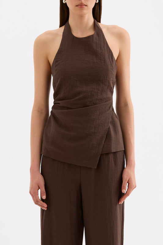 Front close-up showing the high halter neckline, fitted waist and asymmetrical hem styled with matching chocolate pants.