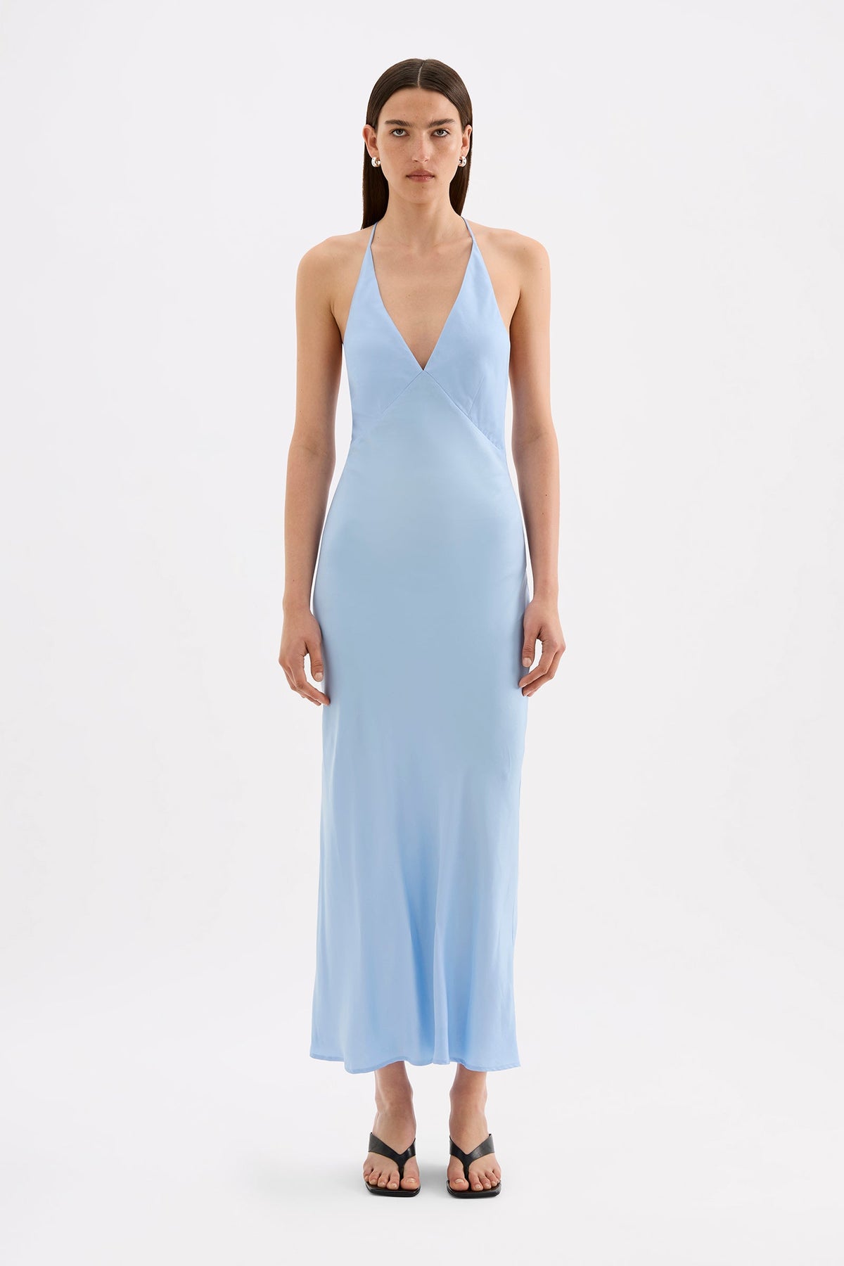 A model wears the Bermuda blue maxi dress in a full front studio view, showing the V neckline, thin straps and flowing ankle-length silhouette.