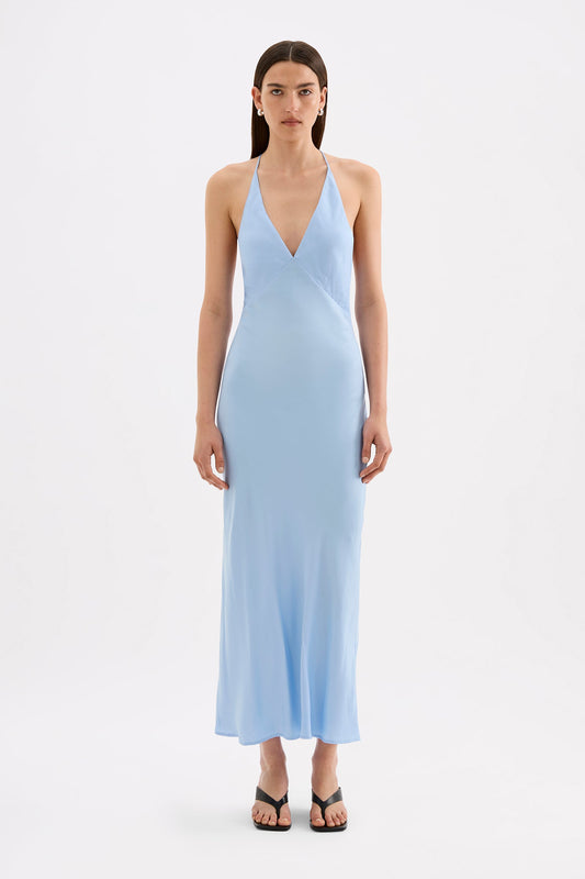 A model wears the Bermuda blue maxi dress in a full front studio view, showing the V neckline, thin straps and flowing ankle-length silhouette.