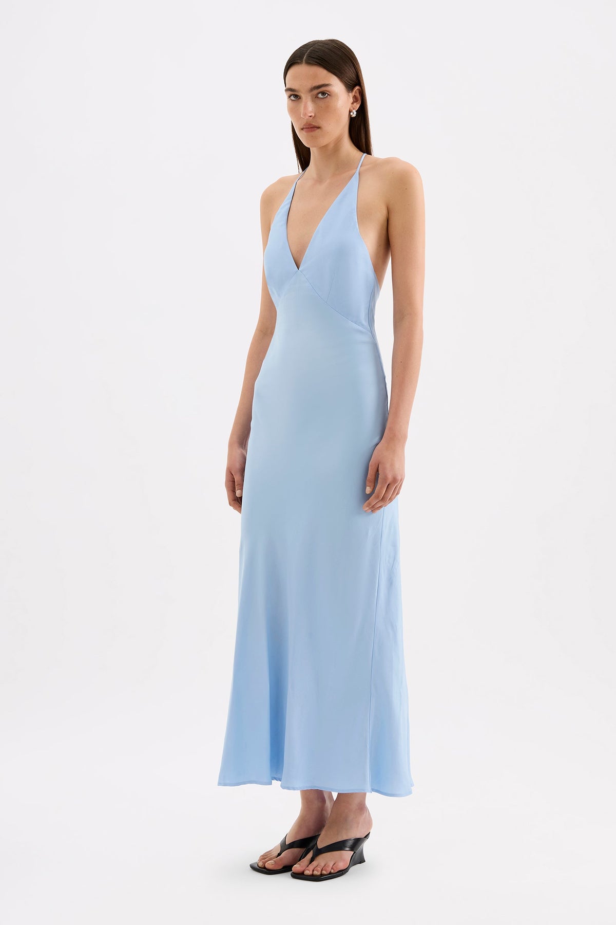 The model wears the Bermuda blue maxi dress in a three-quarter side view, showing the bias-cut shape and flowing skirt.
