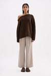 Full-length front view of an oversized chocolate off-shoulder knit styled with wide-leg trousers.