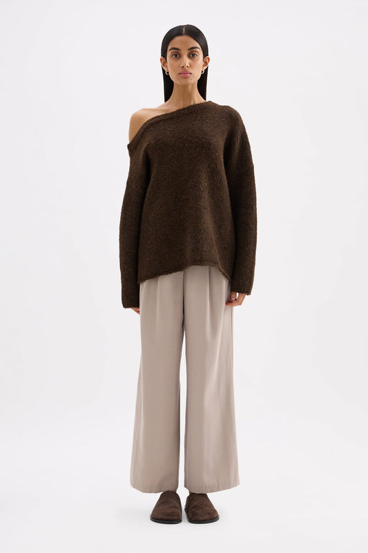 Full-length front view of an oversized chocolate off-shoulder knit styled with wide-leg trousers.