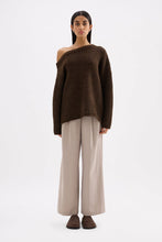 Full-length front view of an oversized chocolate off-shoulder knit styled with wide-leg trousers.