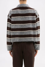 Person wearing a striped sweater with brown, gray, and white horizontal stripes on a plain background.