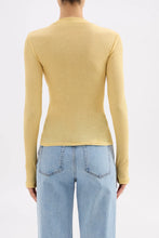 Person wearing a yellow long-sleeve top and light blue jeans on a white background