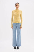 Woman wearing a yellow ruched sweater and light blue jeans on a white background