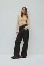Woman wearing a beige top and black pants against a white background