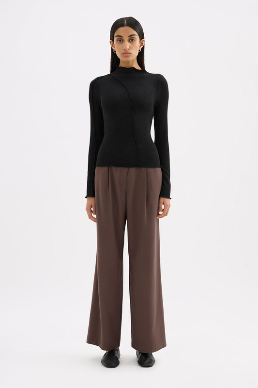 Black fitted long sleeve top styled with brown wide-leg trousers in a full-length front view.