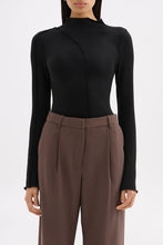 Close front view of the black long sleeve top showing the raised neckline and curved stitching detail.