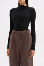 Three-quarter view of the fitted black top highlighting the long sleeves and sculpted seam detailing.
