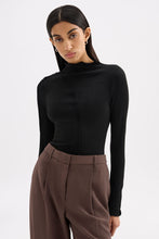 Model wearing the fitted black long sleeve top in a relaxed angled pose with one hand in her trouser pocket.