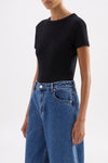 Three-quarter front view of the black fitted tee paired with wide-leg blue jeans in a minimal white studio.