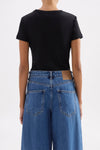 Back view showing the close-fitting silhouette and short sleeves styled with blue denim jeans.