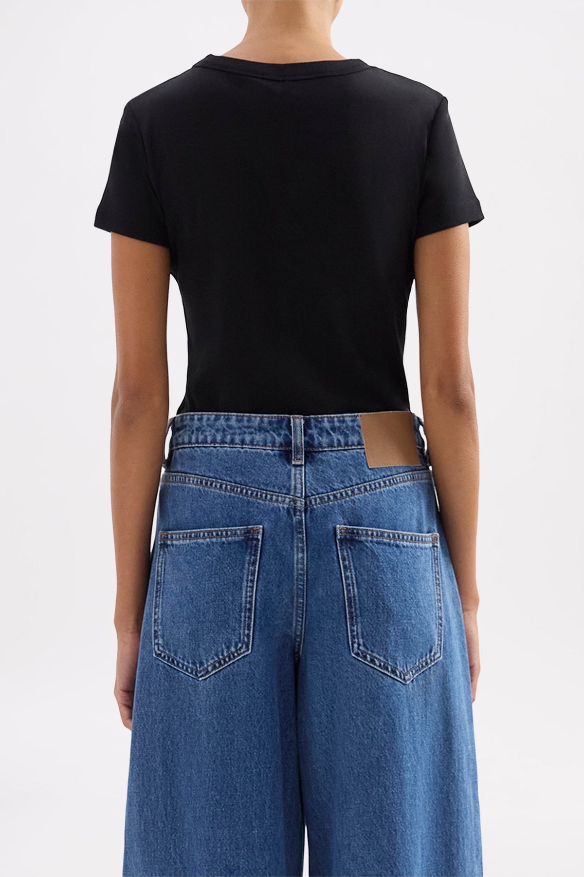 Back view showing the close-fitting silhouette and short sleeves styled with blue denim jeans.