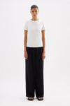 Full-length front view of the fitted white baby tee styled with black wide-leg trousers against a clean studio background.