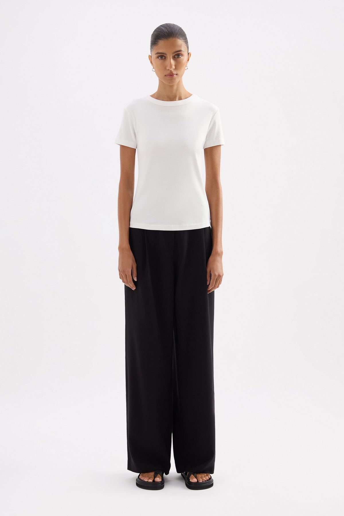 Full-length front view of the fitted white baby tee styled with black wide-leg trousers against a clean studio background.