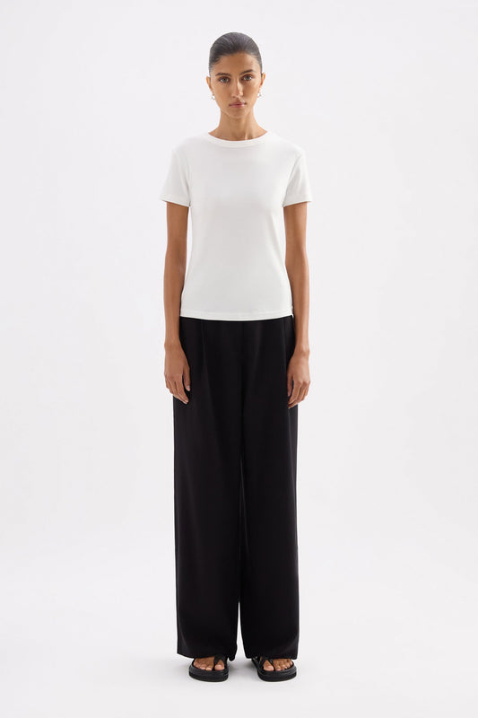 Full-length front view of the fitted white baby tee styled with black wide-leg trousers against a clean studio background.