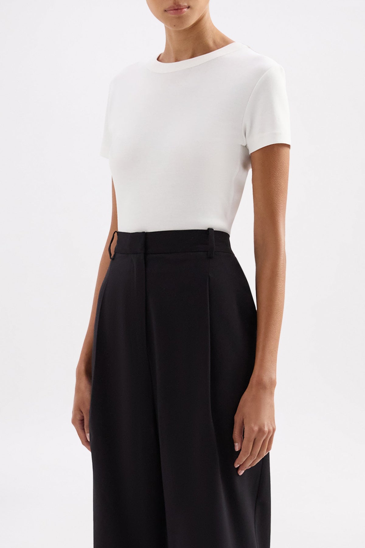 Three-quarter view of the fitted white short sleeve tee styled with black trousers.