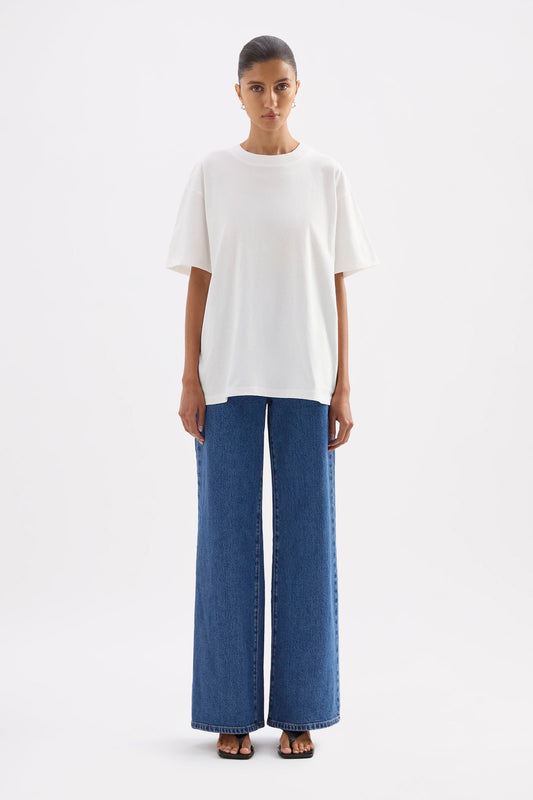 Front full-length view of the oversized white tee styled with wide-leg blue jeans in a clean white studio.