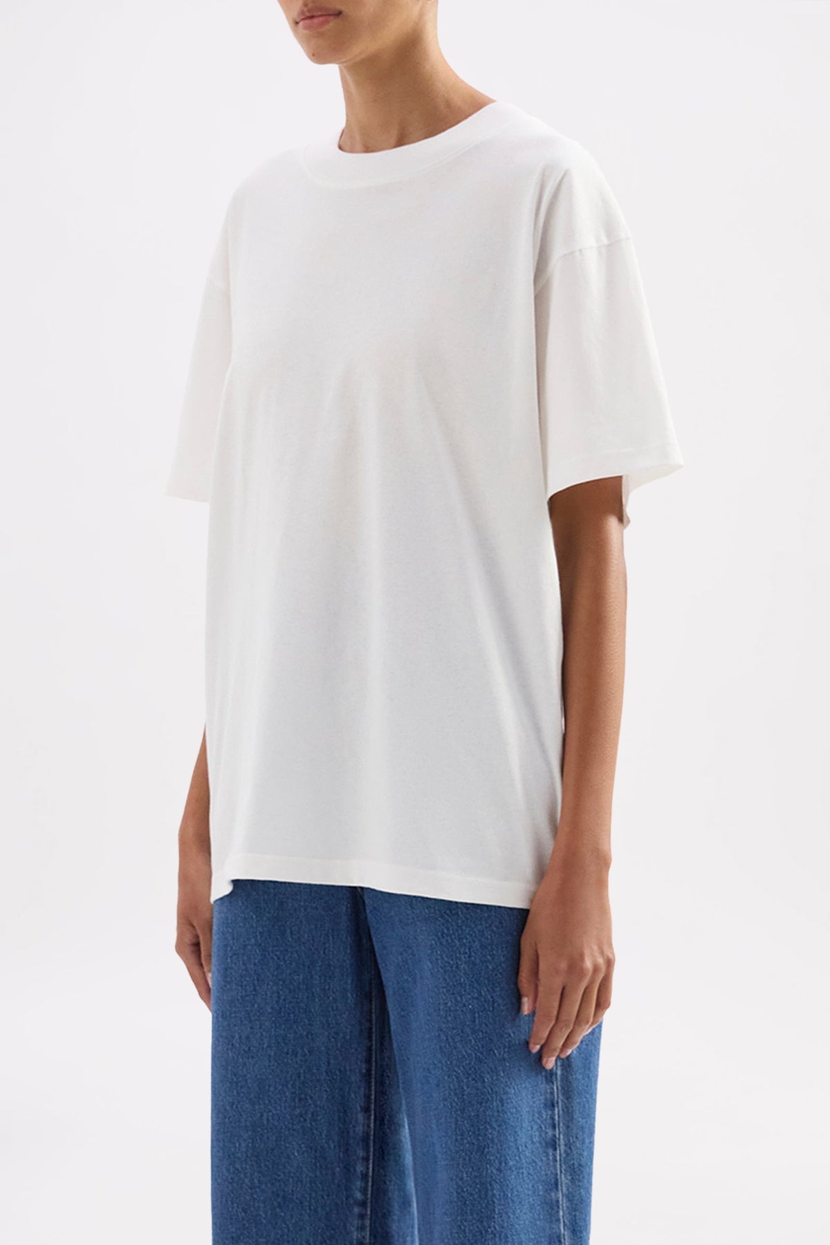 Three-quarter view highlighting the oversized silhouette and dropped shoulder shape styled with blue denim.