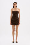 A model wears a chocolate brown mini dress with thin straps and draped detailing through the body in a full front studio view.