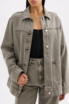 Model wearing the stone grey denim jacket open over a black top with matching jeans in a close front pose.