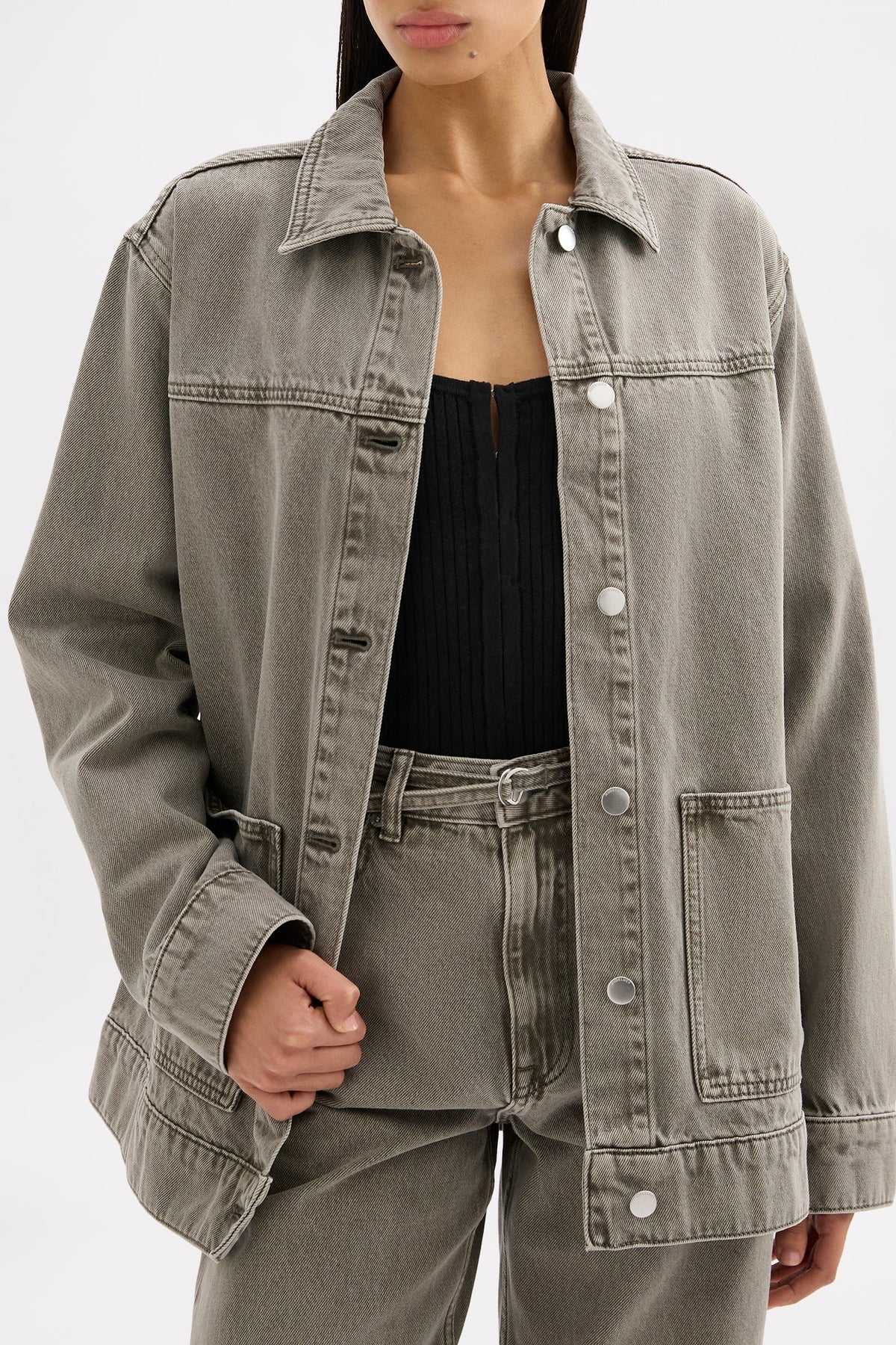 Model wearing the stone grey denim jacket open over a black top with matching jeans in a close front pose.
