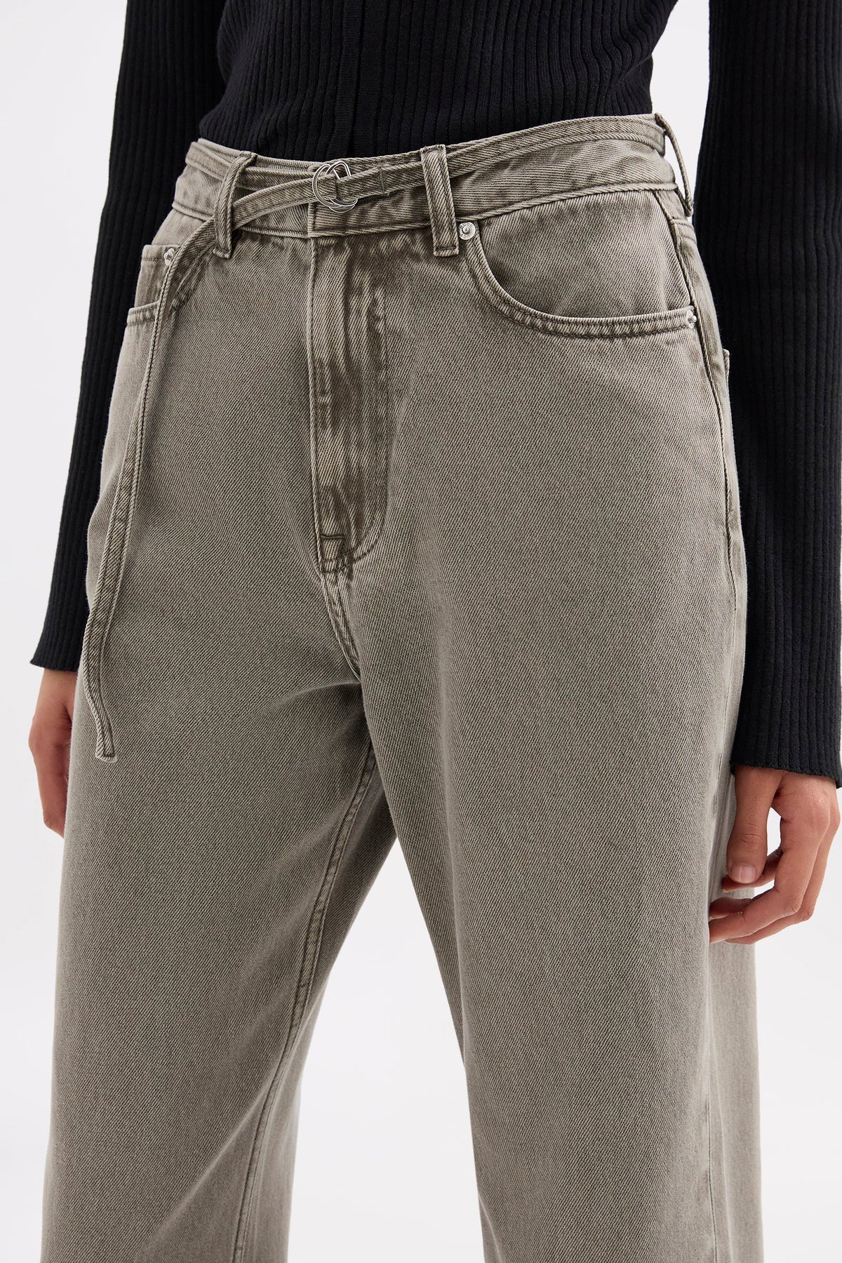 Close front view highlighting the high-rise waistband, button closure, front pockets and narrow denim belt feature.