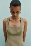 A close-up lifestyle view shows a model wearing the Nude Lucy Thea Top in moss with a square neckline and fitted shape.
