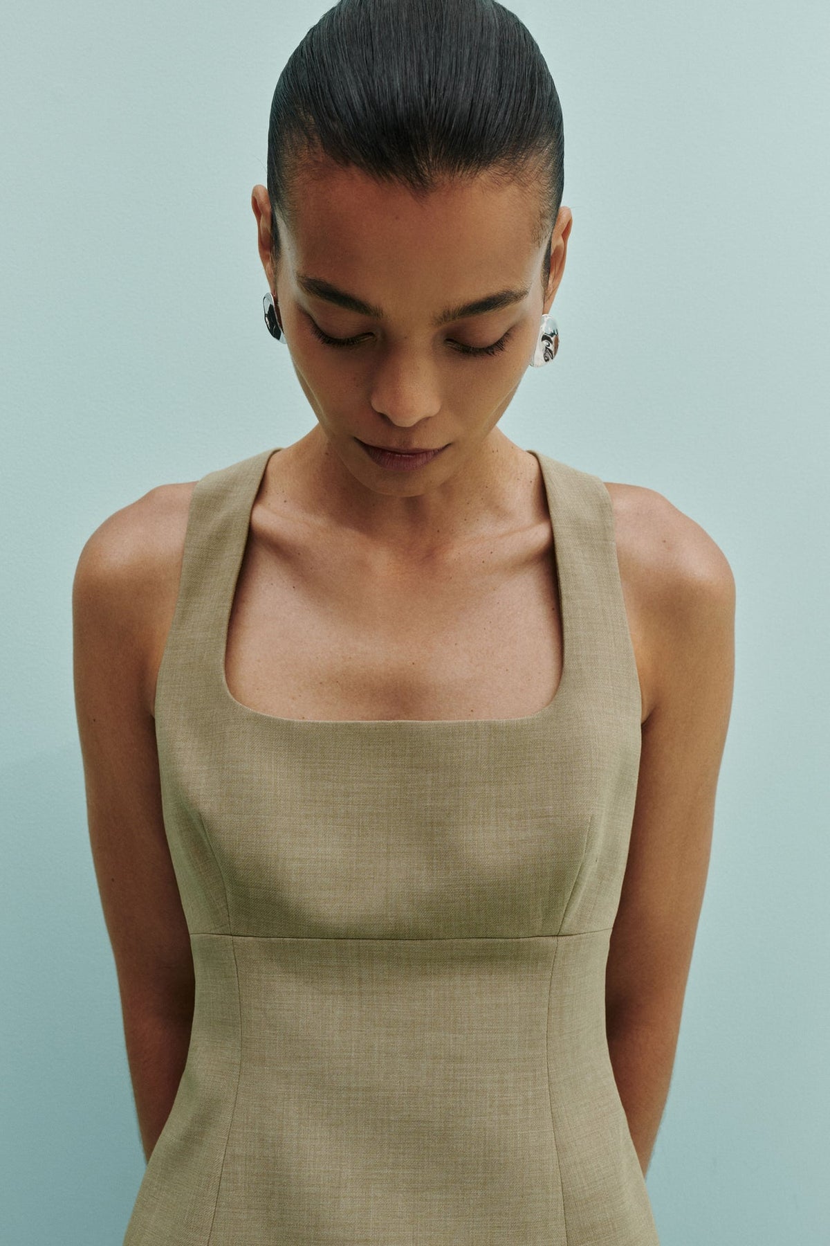 A close-up lifestyle view shows a model wearing the Nude Lucy Thea Top in moss with a square neckline and fitted shape.
